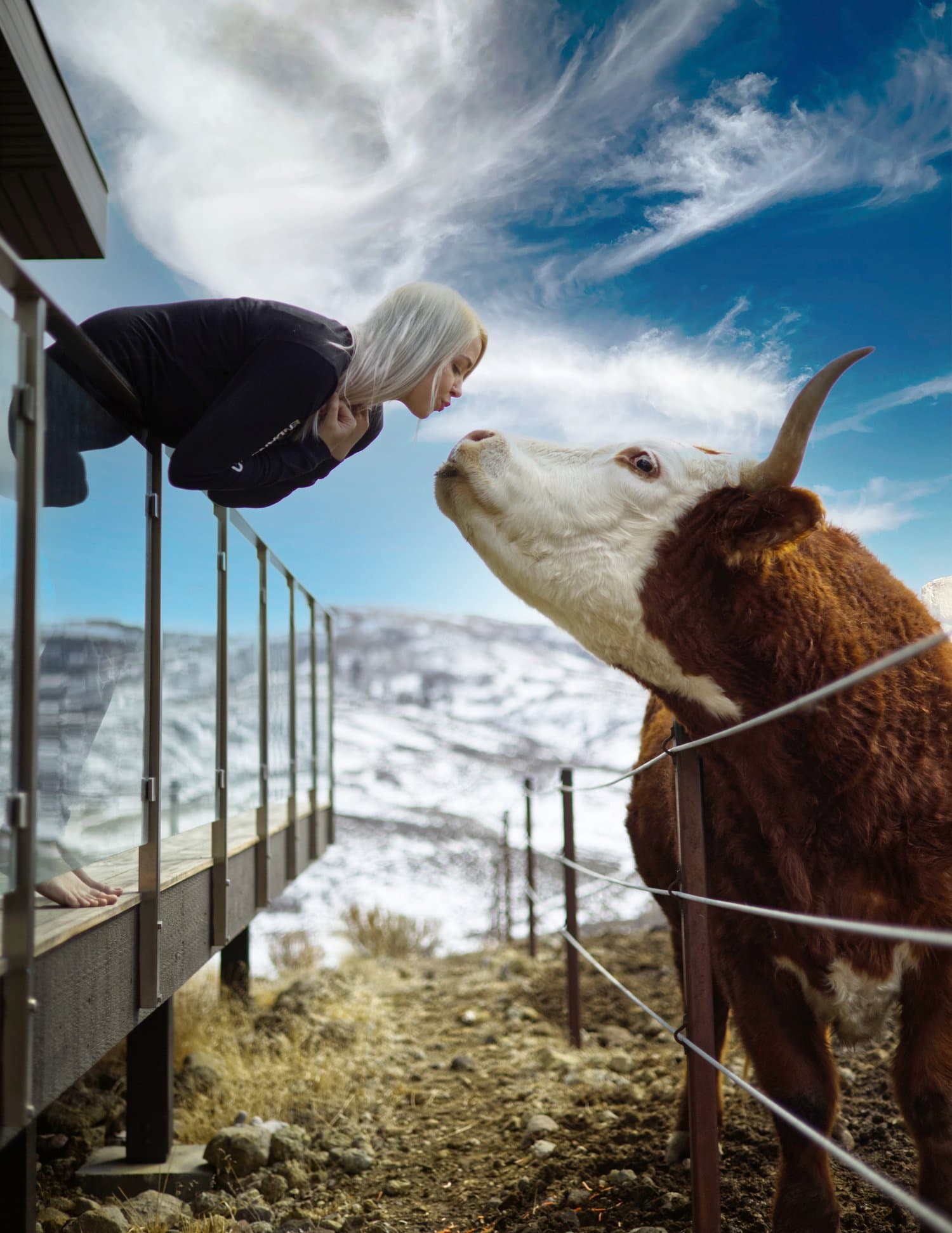 Miranda leaning over a deck railing to kiss Bradley on the nose, with snowy hills behind them